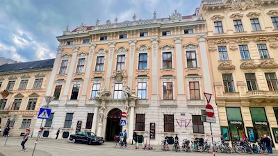 Ein mehrstöckiges Barockpalais mit repräsentativem Portal, mit frei stehenden Statuen am Fassadenabschluss.