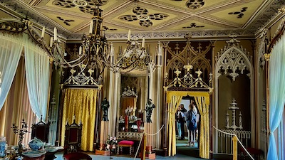 Raum mit gemalten Wandnischen, einer gemalten Kassettendecke, beides die Gotik imitierend. Ein mehrarmiger Luster hängt von der Decke. 