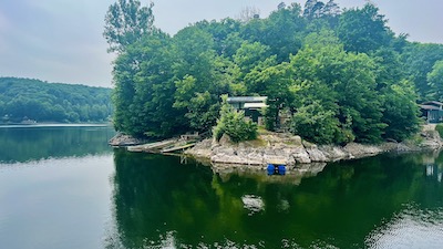 Eine kleine Hütte an einem felsigen Seeufer, inmitten von Bäumen.