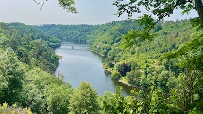 Blick auf einen tief in einem grünen Tal gelegenen Stausee.