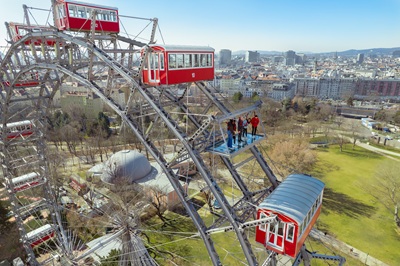 Drohnenaufnahme des Riesenrads mit Menschen auf der Plattform 9 und Wien und der Kaiserwiese im Hintergrund