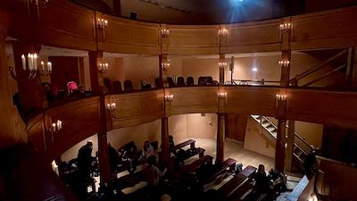 Ein Barocktheater aus Holz mit zwei Logenrängen in abendlicher Beleuchtung.