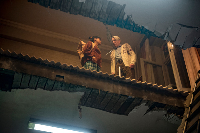Lea (Sira-Anna Faal ) und ihr Opa Oswalt (Axel Werner) blicken von ihrer zertrümmerten Wohnung auf das unterhalb liegende Stockwerk. An den demolierten Boden ist eine Leiter angelehnt.