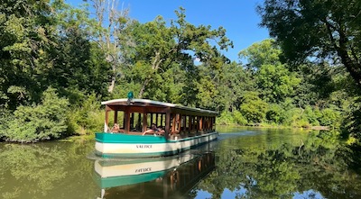 Ein kleines Ausflugsschiff auf einem Kanal, zu beiden Seiten begrünt.
