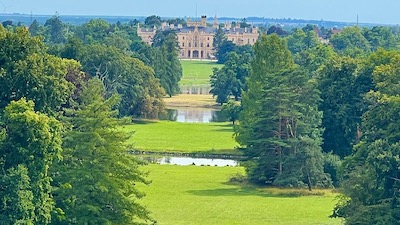 Ein Schloss, davor eine Abfolge von Wiesen und Wasserläufen, gesäumt von Bäumen.