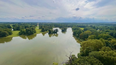 Blick auf den riesigen Teich eines Schlossparks, umgeben von Bäumen.