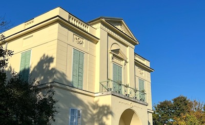 Ein kleines villenartiges Gebäude in klassizistischem Stil vor einem blauen wolkenlosen Himmel.