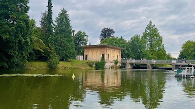 Ein arabisch aussehendes kleines Gebäude an einem Wasserarm, umgeben von verschiedenen Parkbäumen.