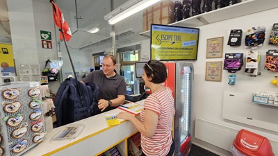 Mann bei der Kassa der Gemeindealpe händigt einer Escape Trail Spielerin den notwendig Rucksack aus
