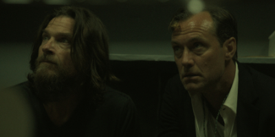 Jude Law und Jason Bateman sitzen in einem düsteren Raum.