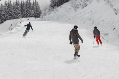 Zwei Skifahrer und ein Snowboarder fahren am Semmering die Piste hinunter.