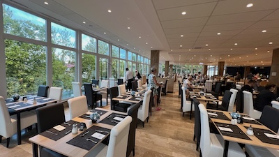 Ein riesiger Speisesaal des Hotels Helios in Hévíz aus den 1970iger Jahren, mit großen Fensterfronten, die von der Decke bis zum Boden reichen.