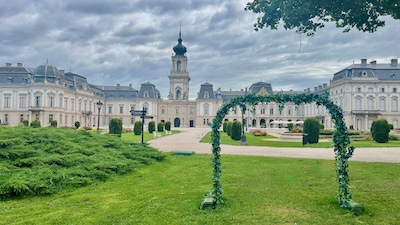 Das neobarocks, langgezogene Schloss Festetics in Keszthely, davor eine grüne Wiese und ein Blumenbogen.