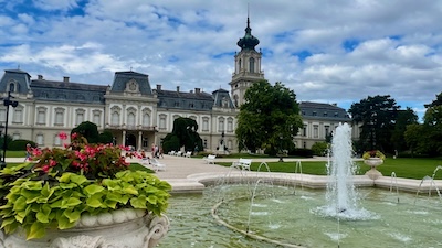 Ein Springbrunnen mit großem Wasserbecken vor einem neobarocken Schloss mit einem Turm, dem Schloss Festetics