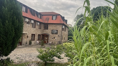 Ein einstöckiger Natursteinbau mit ausgebauter Mansarde, davor ein Garten.
