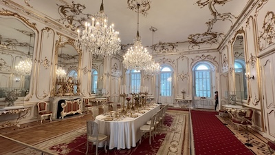 Ein Neobarocker Prunkraum mit zahlreichen Spiegeln, Kristalllustern und einem festlich gedeckten Tisch.