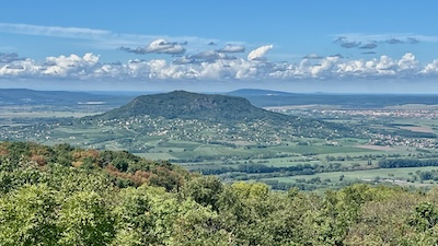 Der Sankt-Georgs-Berg (Szent György-hegy). Ein Tafelberg vulkanischen Ursprungs, bewaldet, in mitten einer grünen Landschaft unter blauem Himmel.