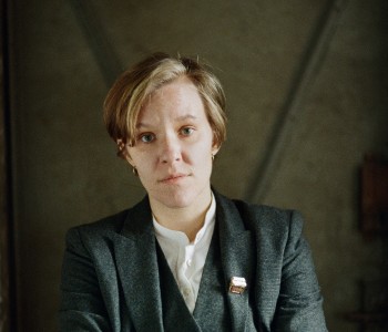 Die Autorin Raphaela Edelbauer in grauem Anzug vor einer Pressholzwand.