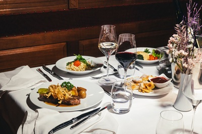 Gedeckter Tisch mit feinem Essen aus Österreich - Beef Tartar, Kaiserschmarrn, Risotto, Rot- und Weißwein.