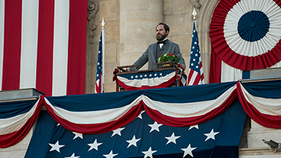 Schauspieler Michael Shannon als Präsident James Garfield in der Netflix-Serie Death by Lightning steht an einem Pult umgeben von amerikanischen Flaggen