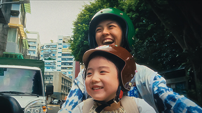 Glückliche Mutter und ihre Tochter lachen in die Kamera während sie auf einem Moped fahren