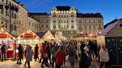 Der Hauptplatz (Hlavné námestie) von Bratislava, in der Mitte das Gebäude der Diskontbank von 1911. Nächtlich beleuchtet, mit Besuchern und Ständen des Weihnachtsmarkts.