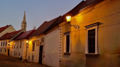 Blick in die nächtlich beleuchtete Kapitulská Gasse von Bratislava. Dahinter der gotische Helm der Klarissenkirche.
