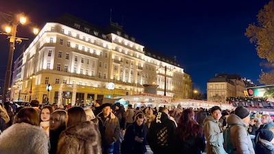 Hotel Carlton in Bratislava in nächtliche Beleuchtung. Davor Menschen am Weihnachtsmarkt.