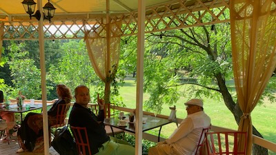 Die Veranda des Cafés Elizabeth in Piešťany. Auf der Kaffeeterrasse sitzen einige Damen und Herren, im Hintergrund eine Wiese und Bäume.