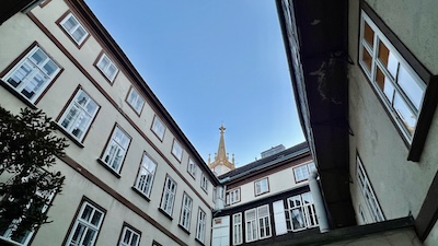 Innenhof des Hauses Augustinerstraße 12 in der Wiener Innenstadt. Blick aus dem Hof in den Himmel. Die Spitze der Augustinerkirche lugt hervor.