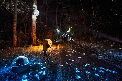 Frau tanzt in einem von Discolichtern beleuchtetem Waldweg