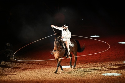 Miguel LaRiata auf einem Pferd mit weißem Anzug und schwarzem Hut und einem Lasso um sich und das Pferd.