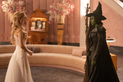 Elphaba und Glinda. Elphaba hat grüne Haut und ein schwarzes Kleid. Glinda hat blonde Haare und ein pinkes Kleid.