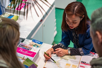Frau erklärt bei der Ferien-Messe auf einer Karte ein Urlaubsziel in Thailand.