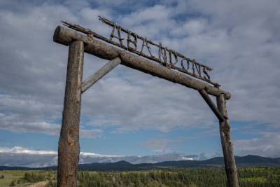ein Holzlogo mit der Aufschrift ABANDONS in Blockbuchstaben, dahinter pittoreske Landschaft mit leicht bewölktem Himmel