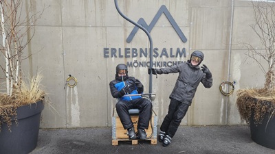 Vater und Sohn posieren auf einem Stück des alten 1er-Sessellifts vor dem Logo der Erlebnisalm Mönichkirchen