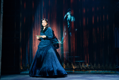 auf der Bühne...dunkelhaarige Frau in dunkelblauem Kleid, einen Brief in der Hand halten, vor einem roten Vorhang stehend, hinter Vorhang: männliche, aristokratisch anmutende männliche Gestalt 