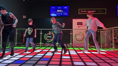 Zwei Buben, ein Mädchen und eine Frau bewegen sich auf bunt beleuchteten Bodenwürfeln bei den Pixel Games im Wiener Prater.