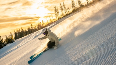 Skifahrer carvt mit tiefer Sonne im Hintergrund, der Schnee spritzt auf. Auf der schwarzen Piste bei der Abfahrt nach Mariensee