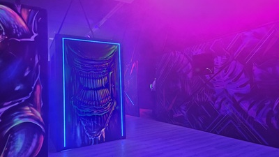 Mit Blacklight-Farben bemalte Wände auf dem ein Xenomorph-Alien die Zähne fletscht.