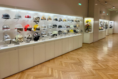 Ausgestellte Wiener Feuerwehrhelme aus verschiedenen Epochen in unterschiedlichen Farben an einer Wandvitrine