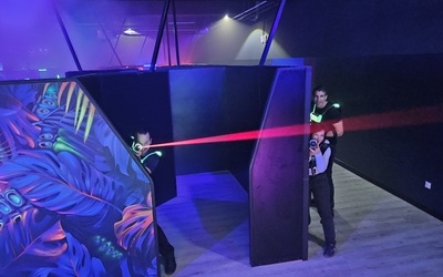 3 Personen in Deckung bei einem Lasertag-Spiel. Eine feuert einen Laserstrahl mit seinem Phaser