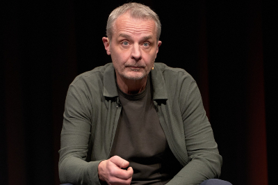 Thomas Maurer in khakifarbener Jacke und grauem Shirt, sitzend, die Hand zu einer halben Faust geballt