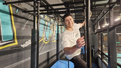 Mann mit Brille klettert an Stangen entlang bei einem Ninja Warrior Parcours