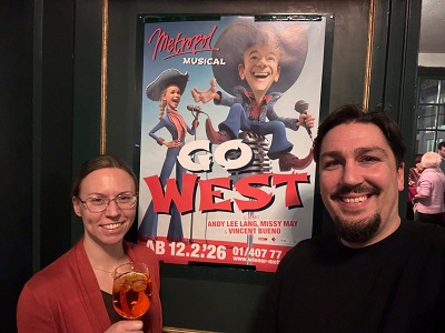 Lächelndes Paar vor Go West Plakat