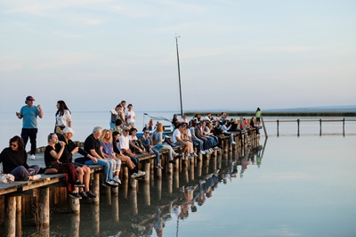 Menschen sitzen beim See Opening in Breitenbrunn am Steg und lassen die Füße baumeln