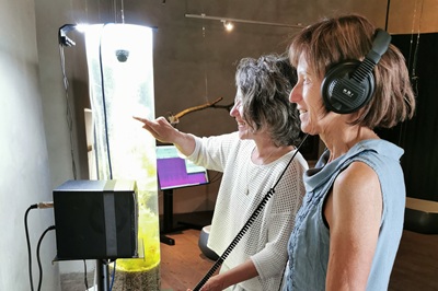 Zwei Frauen, eine mit Kopfhörer, vor einer Audiostation im Aussichtsturm von Schloss Orth