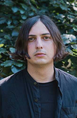 Autor Elias Hirschl vor grüner Blätterwand.