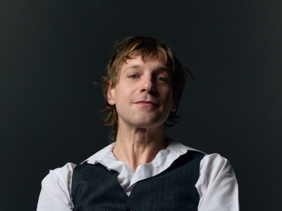 Austro-Sänger und Liedermacher Voodoo Jürgens lächelnd vor einer dunklen Wand