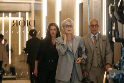 Meryl Streep, Stanley Tucci und Anne Hathaway in Anzügen vor einer Glaswand mit Schriftzug "Dior"